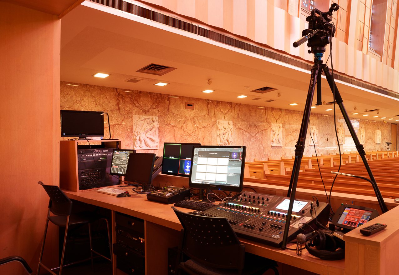Cathedral control booth with video switcher, audio console and camera overlooking the pews