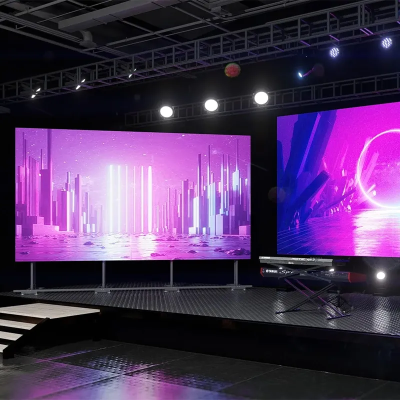 A stage backed by large LED screens displaying vivid visuals, with keyboards and a lighting truss